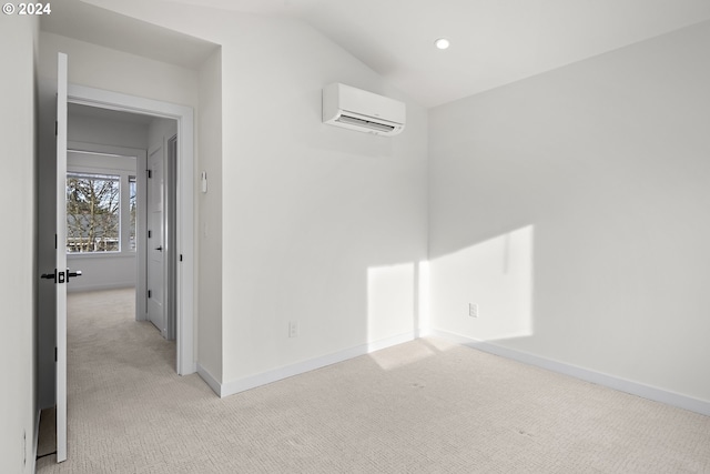 empty room with light colored carpet, a wall unit AC, and vaulted ceiling