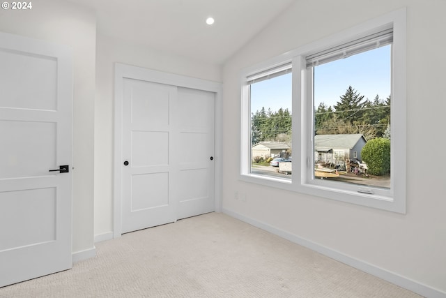 unfurnished bedroom with vaulted ceiling, light colored carpet, and a closet