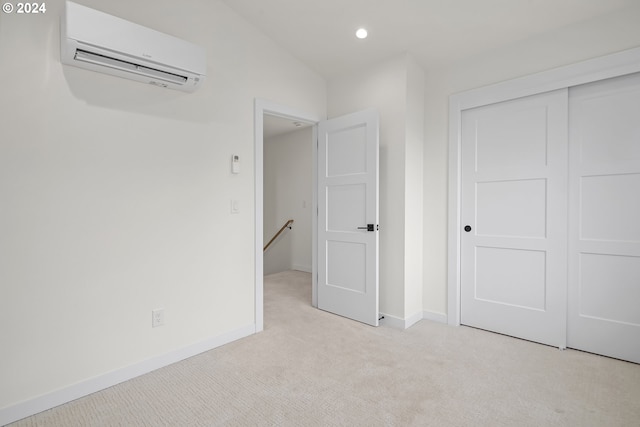 unfurnished bedroom with an AC wall unit, a closet, and light colored carpet