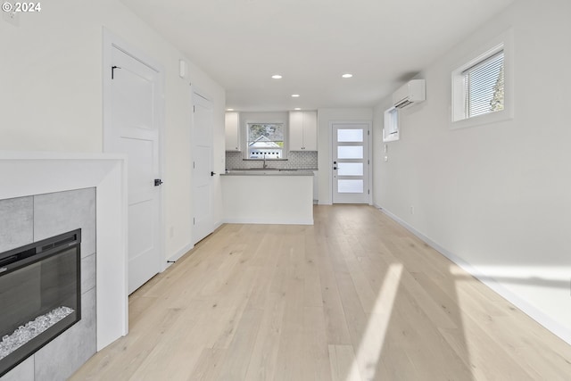 unfurnished living room with a wall mounted air conditioner, light hardwood / wood-style floors, and a fireplace