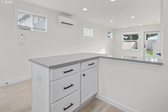 kitchen featuring kitchen peninsula, white cabinets, a wall mounted AC, and light hardwood / wood-style floors