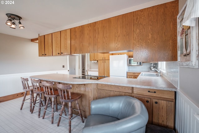 kitchen featuring white refrigerator, sink, a kitchen breakfast bar, kitchen peninsula, and black electric cooktop