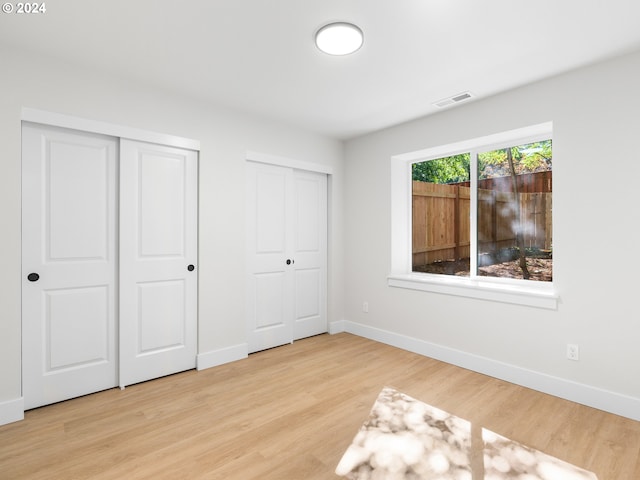 unfurnished bedroom with light wood-type flooring and multiple closets