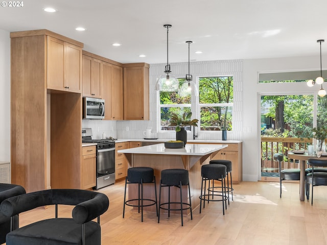 kitchen with pendant lighting, appliances with stainless steel finishes, light hardwood / wood-style flooring, and a kitchen island