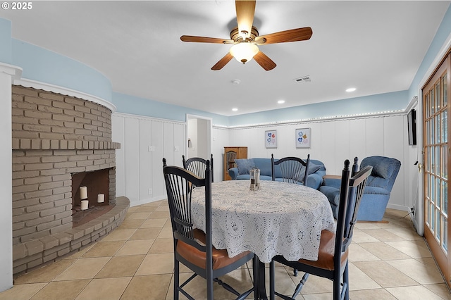 tiled dining room featuring ceiling fan and a fireplace