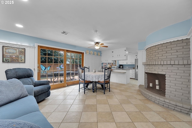 living room featuring a brick fireplace, light tile patterned floors, and ceiling fan