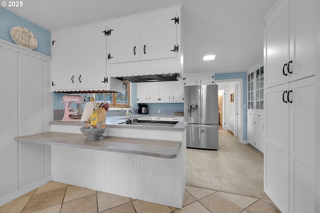 kitchen with light tile patterned flooring, gas cooktop, stainless steel fridge, kitchen peninsula, and white cabinets