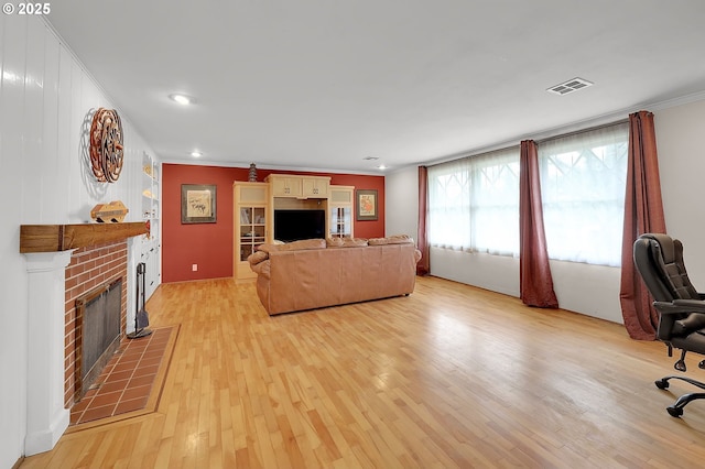 living room featuring crown molding, a fireplace, and light hardwood / wood-style flooring