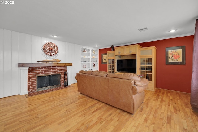 living room with built in features, ornamental molding, a brick fireplace, and light wood-type flooring