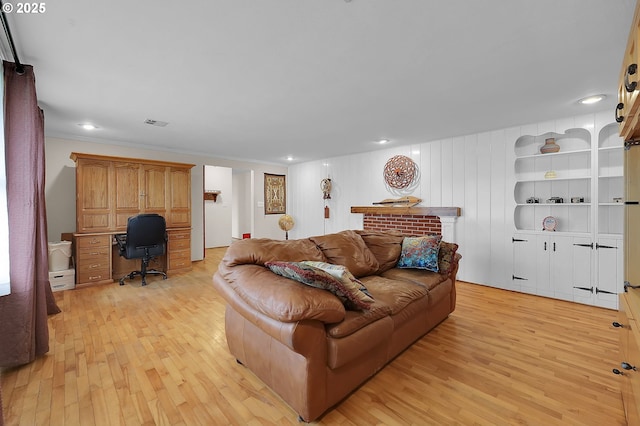 living room featuring built in shelves, ornamental molding, and light hardwood / wood-style floors