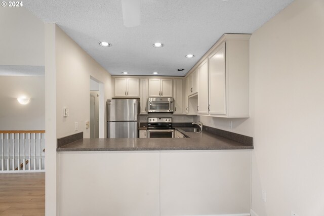 kitchen with kitchen peninsula, appliances with stainless steel finishes, a textured ceiling, light wood-type flooring, and sink