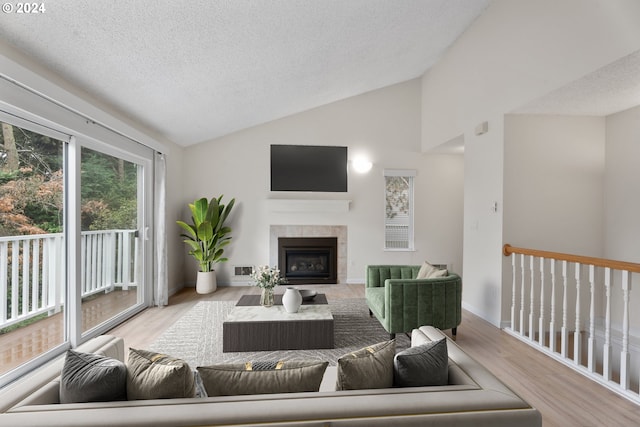 living room featuring light hardwood / wood-style flooring, a textured ceiling, a tiled fireplace, and high vaulted ceiling