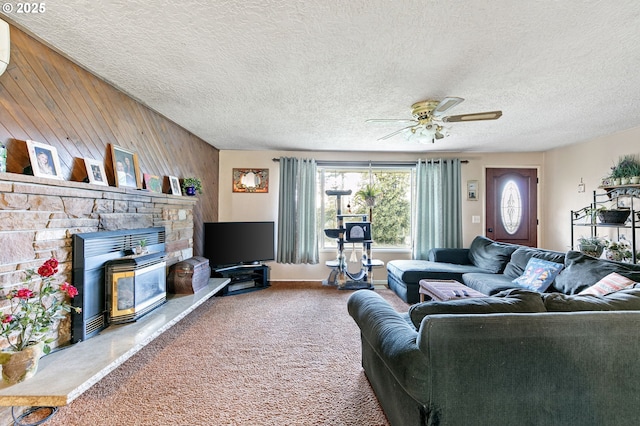 carpeted living room with ceiling fan, wooden walls, a textured ceiling, and a fireplace