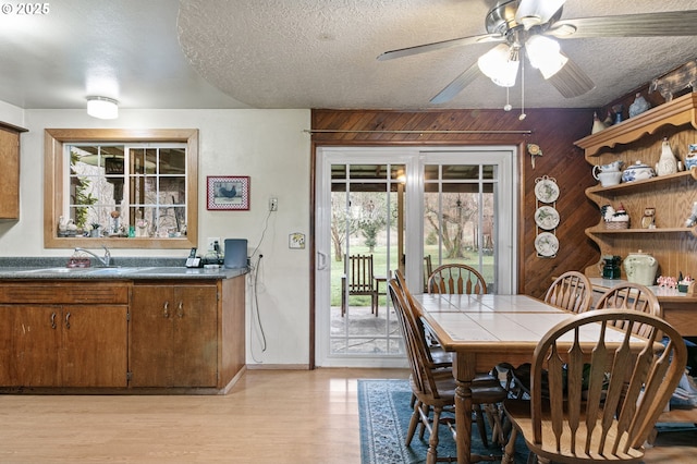 dining room featuring a textured ceiling, ceiling fan, wooden walls, and sink