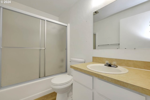 full bathroom with shower / bath combination with glass door, hardwood / wood-style floors, toilet, and vanity