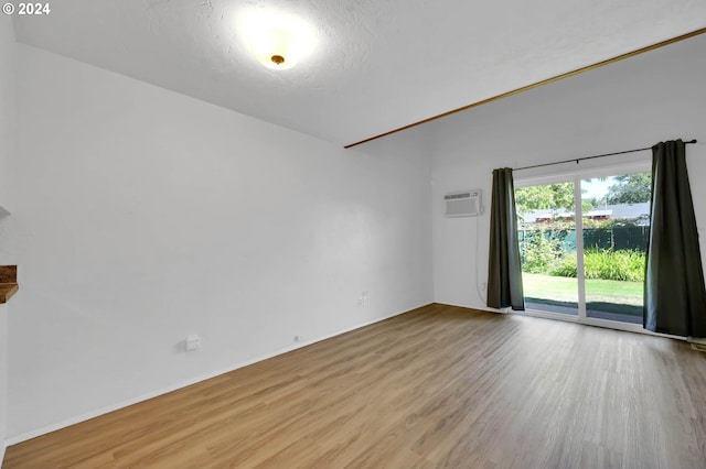 unfurnished room with light wood-type flooring, a textured ceiling, and a wall unit AC