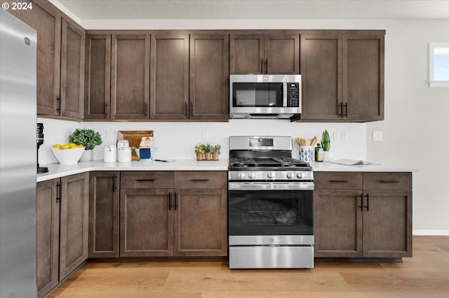 kitchen with appliances with stainless steel finishes, backsplash, light hardwood / wood-style floors, and dark brown cabinets