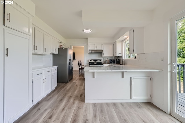 kitchen with appliances with stainless steel finishes, a peninsula, light countertops, under cabinet range hood, and white cabinetry