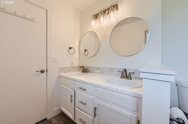 bathroom with double vanity, toilet, backsplash, and a sink