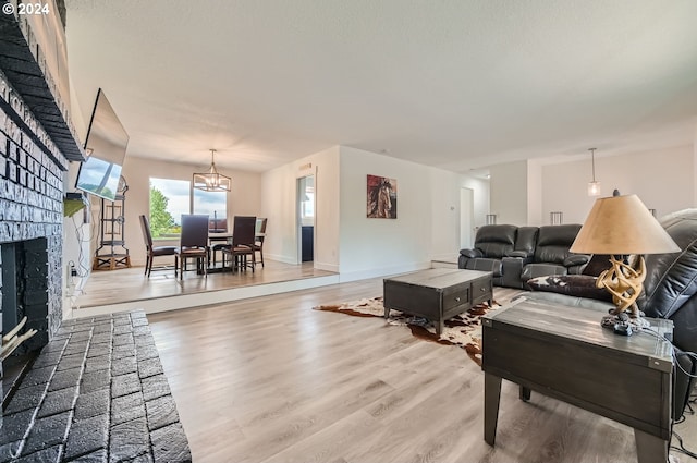 living area featuring a chandelier, a brick fireplace, wood finished floors, and baseboards