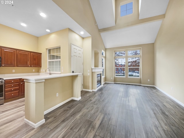 kitchen featuring hardwood / wood-style floors, high vaulted ceiling, a kitchen breakfast bar, stainless steel stove, and kitchen peninsula