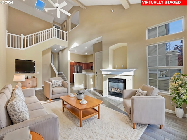 living room with ceiling fan, beamed ceiling, high vaulted ceiling, and light hardwood / wood-style floors