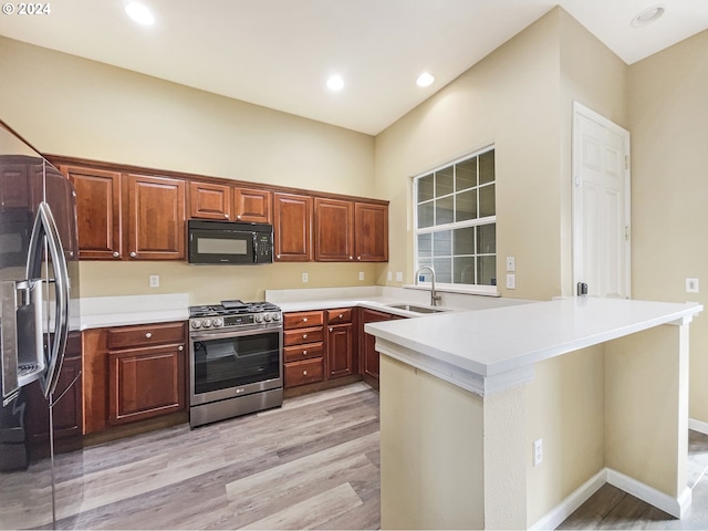 kitchen with kitchen peninsula, gas stove, sink, light hardwood / wood-style floors, and fridge