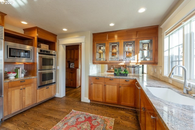 kitchen with stainless steel appliances, light stone countertops, sink, and dark wood-type flooring