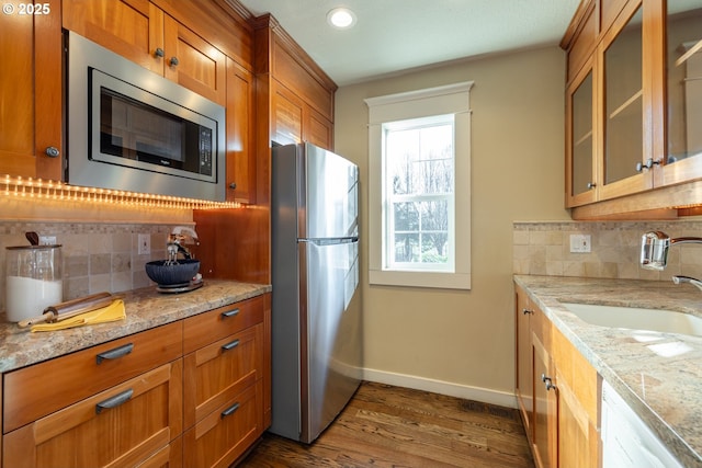 kitchen featuring sink, appliances with stainless steel finishes, backsplash, light stone countertops, and dark hardwood / wood-style flooring