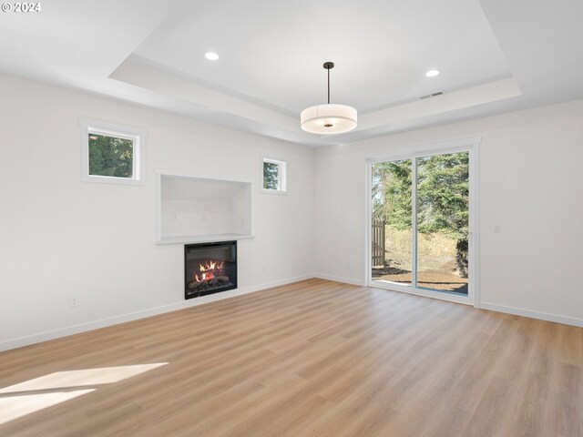 unfurnished living room with light hardwood / wood-style floors, a multi sided fireplace, and a tray ceiling