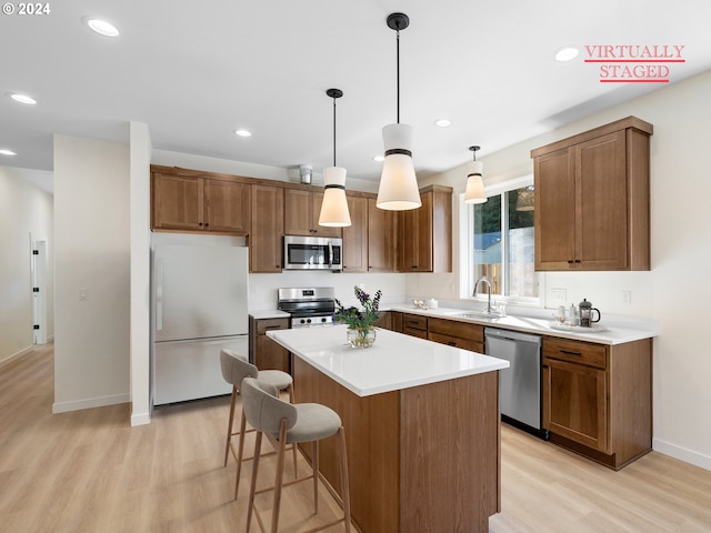 kitchen with sink, a center island, hanging light fixtures, light wood-type flooring, and stainless steel appliances