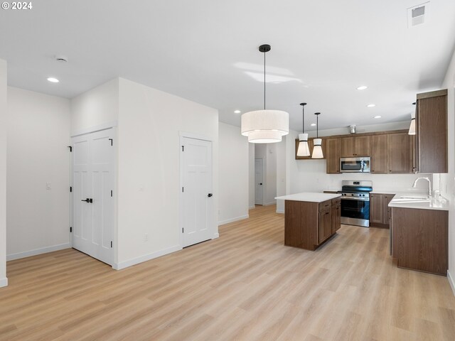 kitchen featuring stainless steel appliances, sink, light wood-type flooring, hanging light fixtures, and a kitchen island