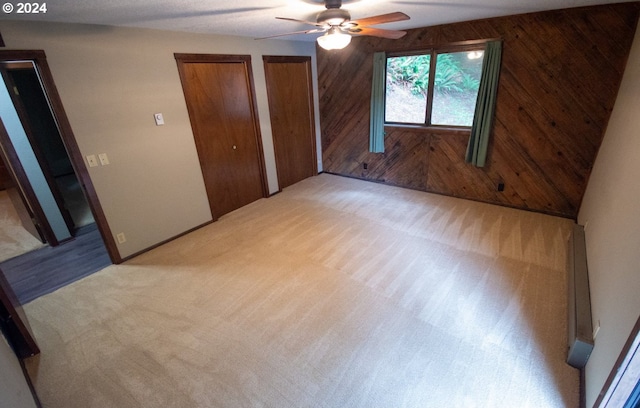 unfurnished bedroom with multiple closets, ceiling fan, wooden walls, and light carpet