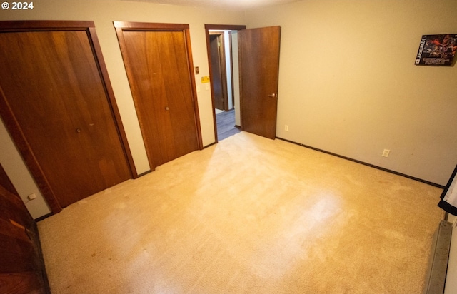 unfurnished bedroom featuring light carpet and multiple closets