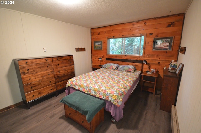 bedroom with wooden walls, dark hardwood / wood-style flooring, a textured ceiling, and a baseboard heating unit