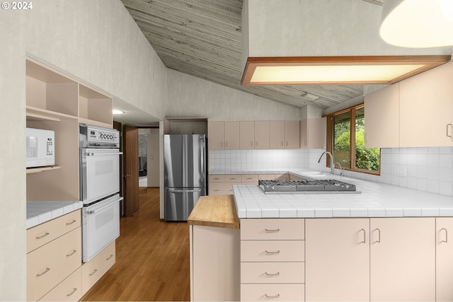 kitchen with lofted ceiling, a peninsula, white appliances, wood finished floors, and decorative backsplash