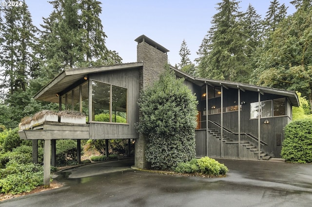 view of property exterior with driveway, stairway, a chimney, and a sunroom