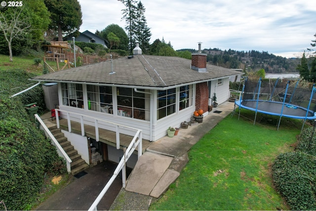 rear view of property featuring a sunroom, a yard, a garage, and a trampoline