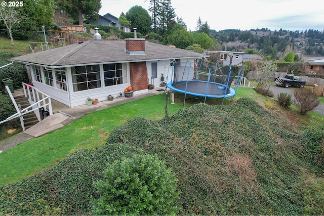 back of property featuring a sunroom, a trampoline, and a lawn