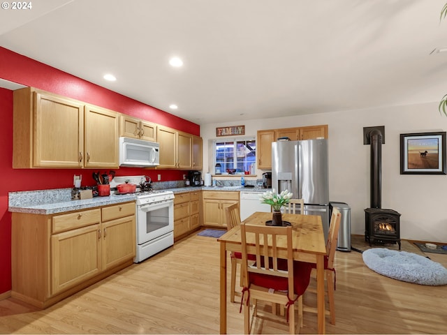 kitchen featuring light hardwood / wood-style flooring, a wood stove, white appliances, and light brown cabinetry