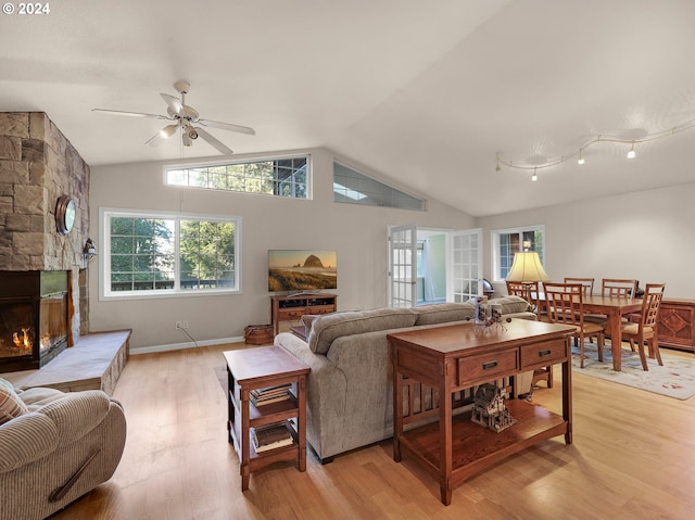 living room with lofted ceiling, light hardwood / wood-style floors, ceiling fan, and a stone fireplace