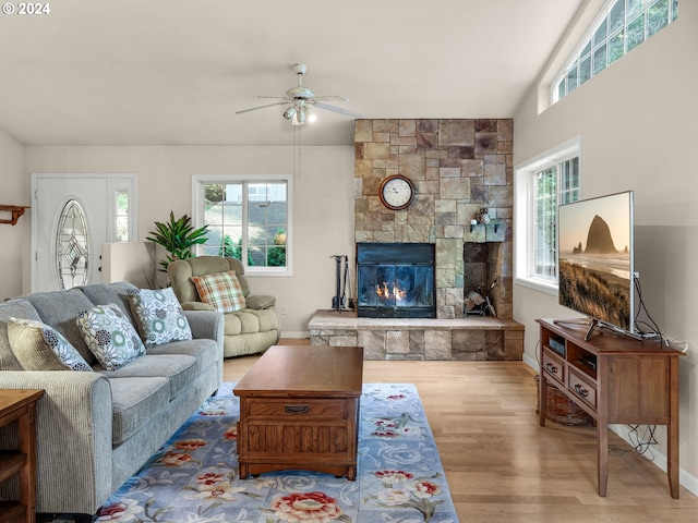 living room with wood-type flooring, a stone fireplace, lofted ceiling, and ceiling fan