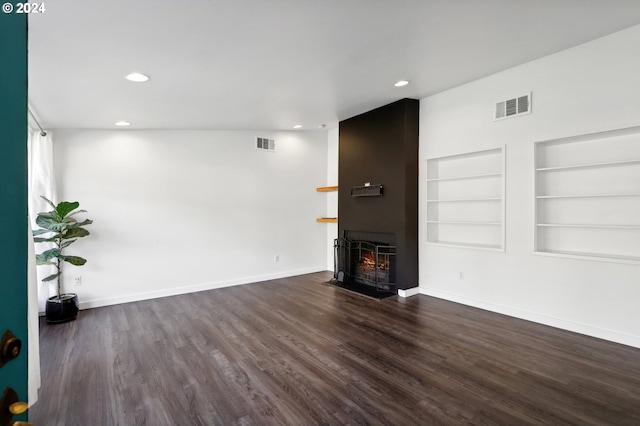 unfurnished living room featuring built in shelves, a large fireplace, and dark wood-type flooring