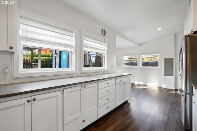 kitchen with lofted ceiling, dark wood-type flooring, electric panel, stainless steel fridge, and white cabinetry