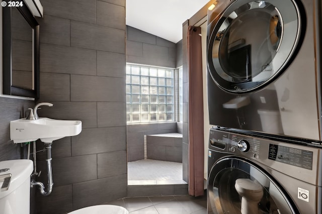 bathroom with tile patterned floors, tile walls, toilet, stacked washer / drying machine, and lofted ceiling