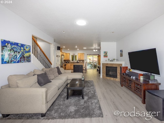 living room with a tiled fireplace, a textured ceiling, and light hardwood / wood-style flooring