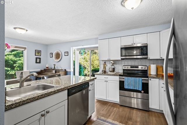 kitchen featuring decorative backsplash, white cabinets, appliances with stainless steel finishes, dark stone countertops, and sink