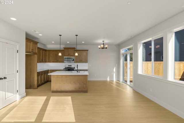 kitchen featuring stainless steel appliances, light countertops, hanging light fixtures, brown cabinetry, and a kitchen island with sink