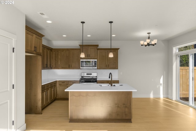 kitchen featuring a center island with sink, appliances with stainless steel finishes, light countertops, pendant lighting, and a sink