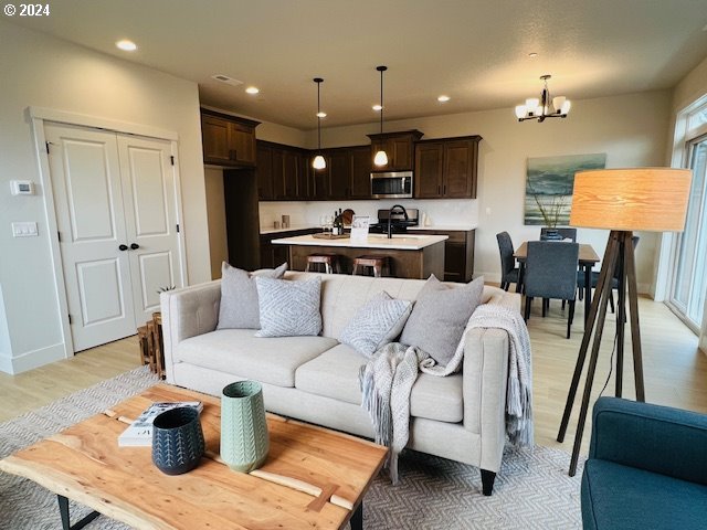 living area featuring baseboards, recessed lighting, light wood-style flooring, and a notable chandelier